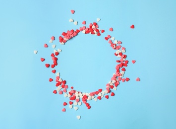 Photo of Round frame made of bright heart shaped sprinkles on light blue background, flat lay. Space for text