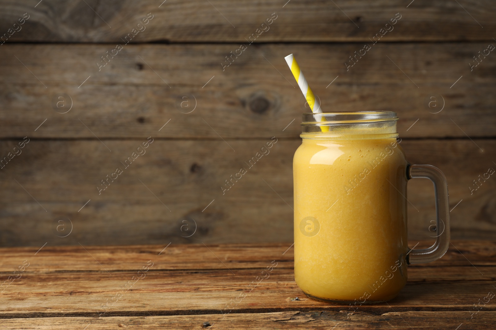 Photo of Mason jar with delicious fruit smoothie on wooden table. Space for text