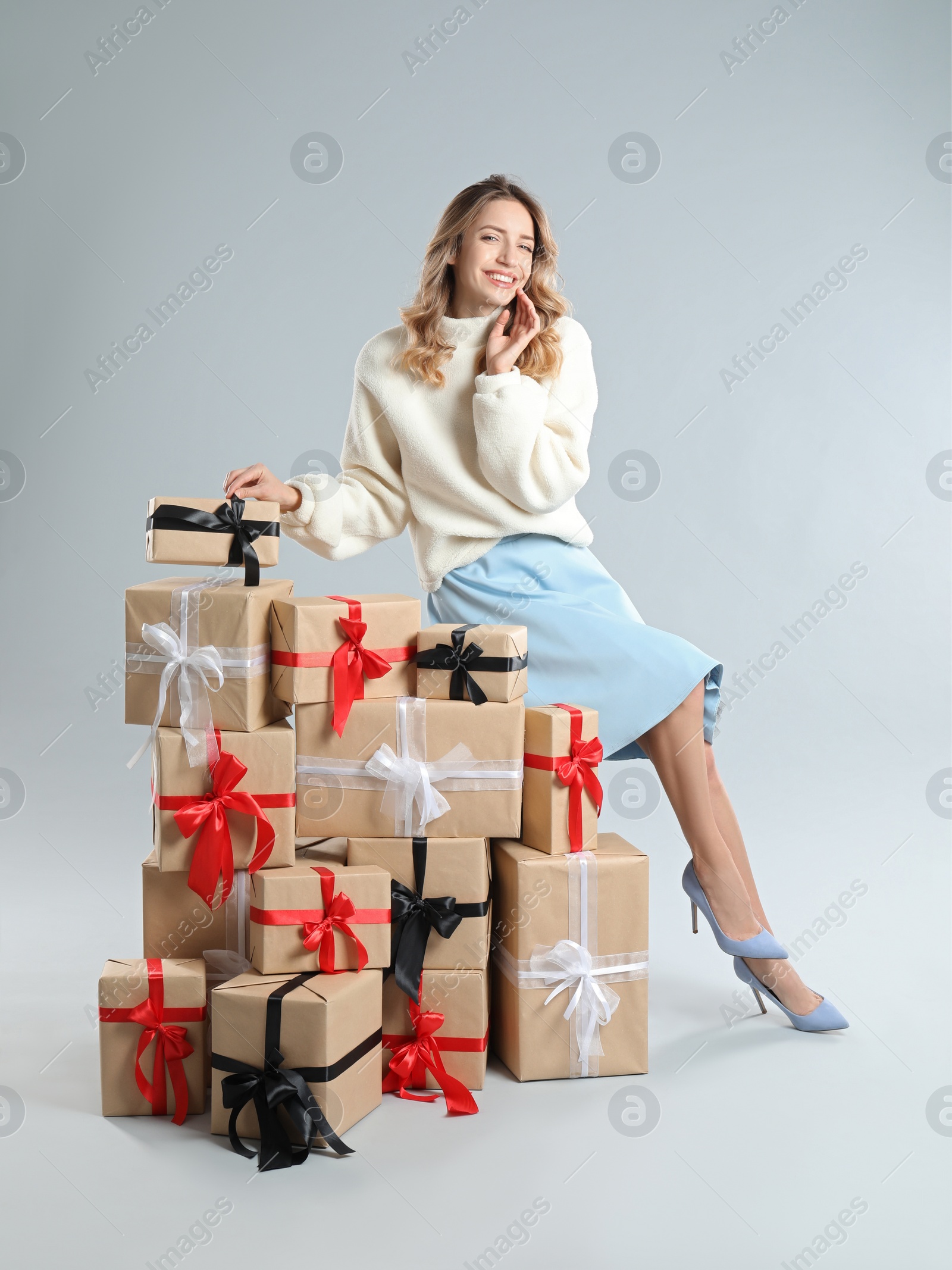 Photo of Beautiful young woman with pile of Christmas presents on light grey background