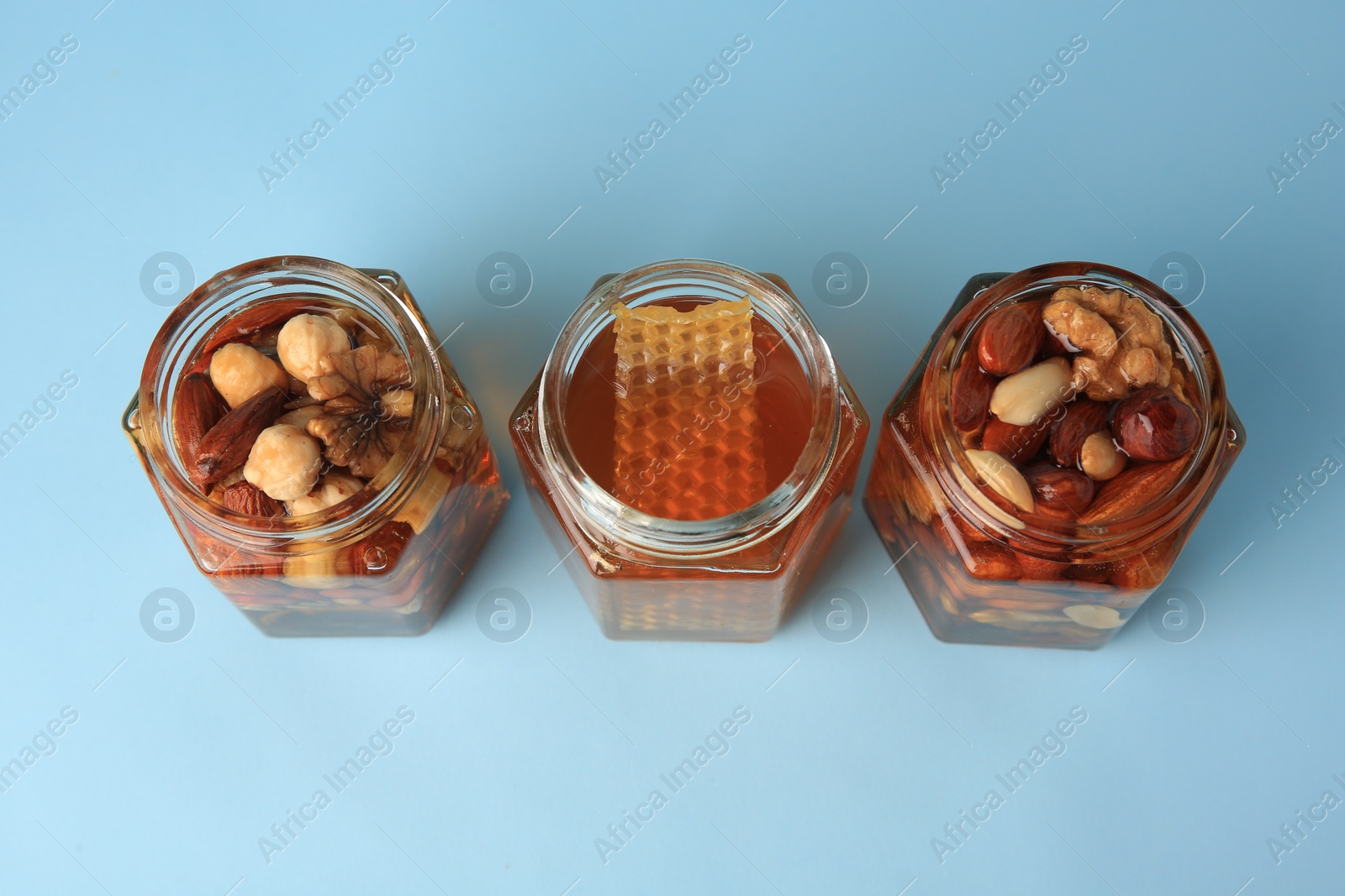 Photo of Jars with different nuts and honey on light blue background, above view