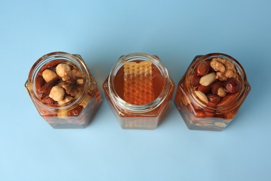 Jars with different nuts and honey on light blue background, above view