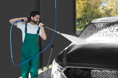 Photo of Worker washing auto with high pressure water jet at outdoor car wash