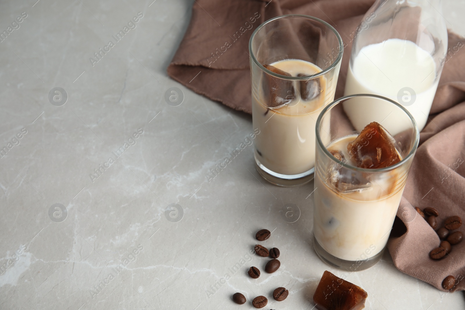 Photo of Glasses of milk with coffee ice cubes on grey table. Space for text