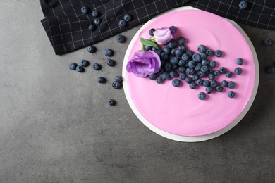 Tasty blueberry cake decorated with flowers on grey table, flat lay. Space for text