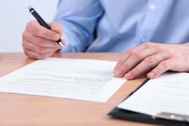 Photo of Businessman signing contract at wooden table, closeup of hands