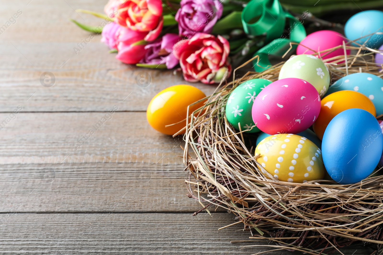 Photo of Bright painted eggs and spring tulips on wooden table, closeup view with space for text. Happy Easter