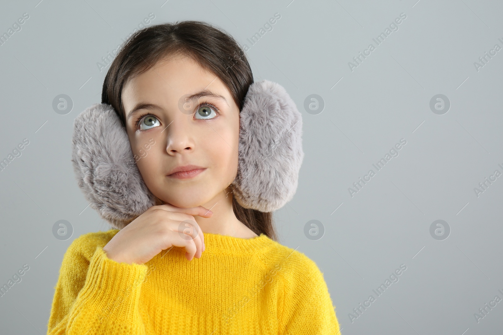 Photo of Cute girl wearing stylish earmuffs on grey background. Space for text