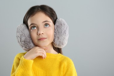 Cute girl wearing stylish earmuffs on grey background. Space for text