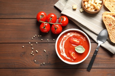 Fresh homemade tomato soup served with bread and croutons on wooden table, top view. Space for text