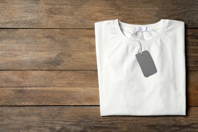Photo of Stylish white T-shirt with label on wooden table, top view. Space for text