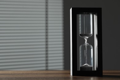 Hourglass with flowing sand on wooden table, space for text