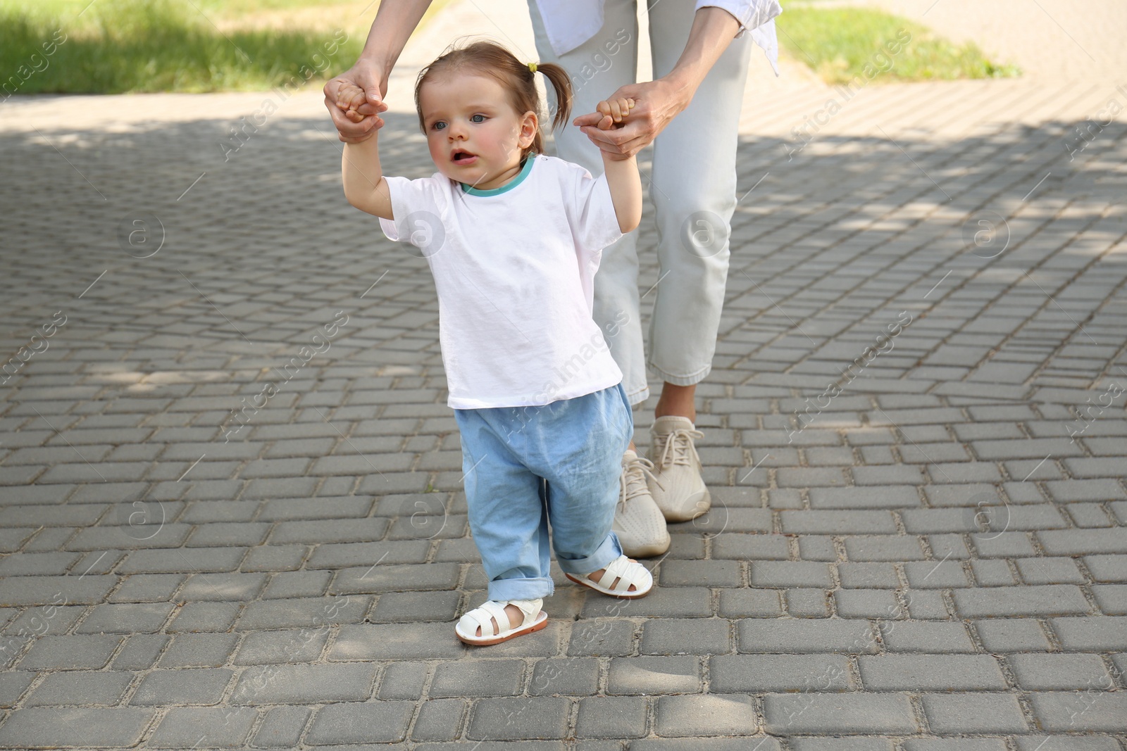 Photo of Mother supporting daughter while she learning to walk outdoors, closeup