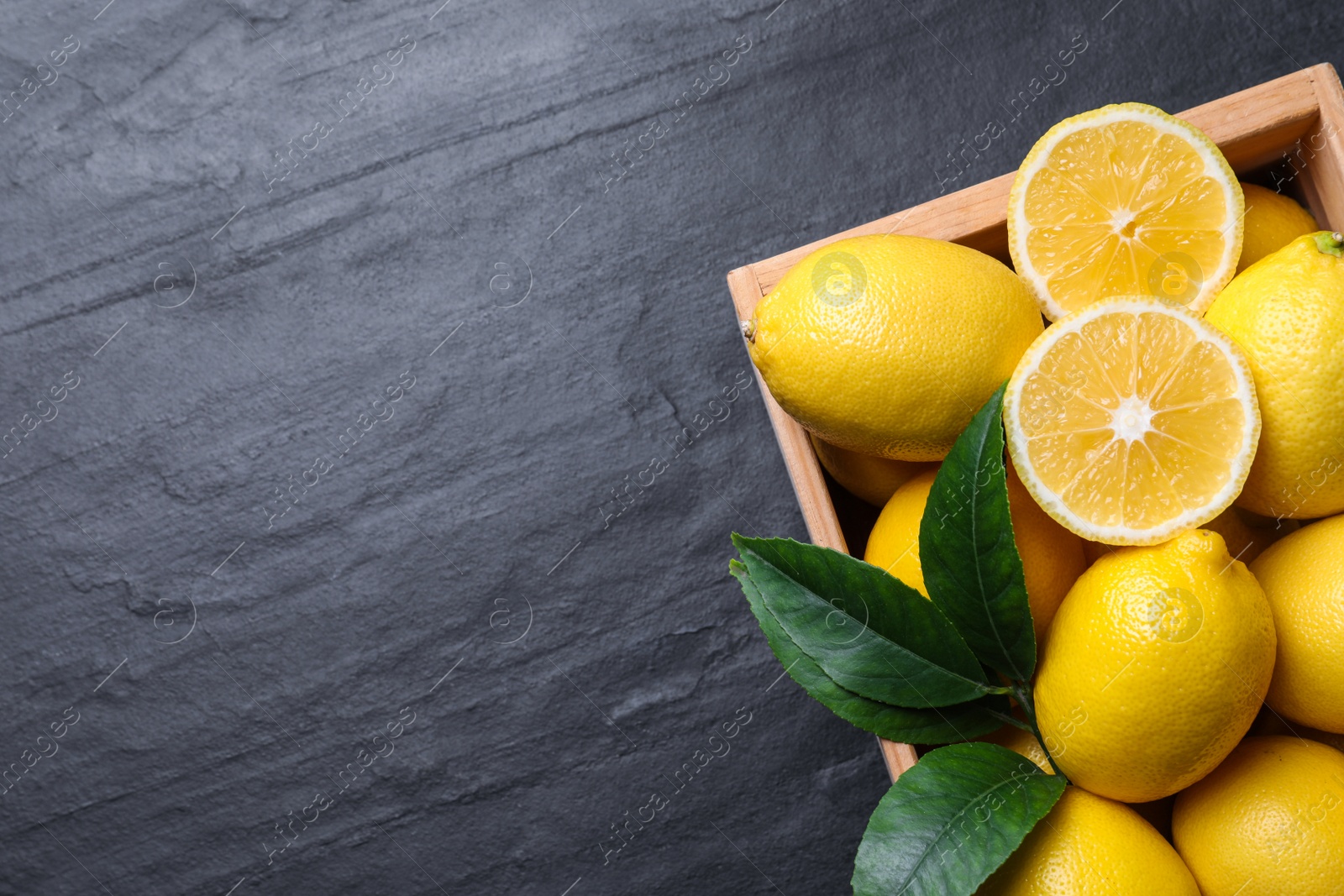 Photo of Many fresh ripe lemons with green leaves on black table, top view. Space for text