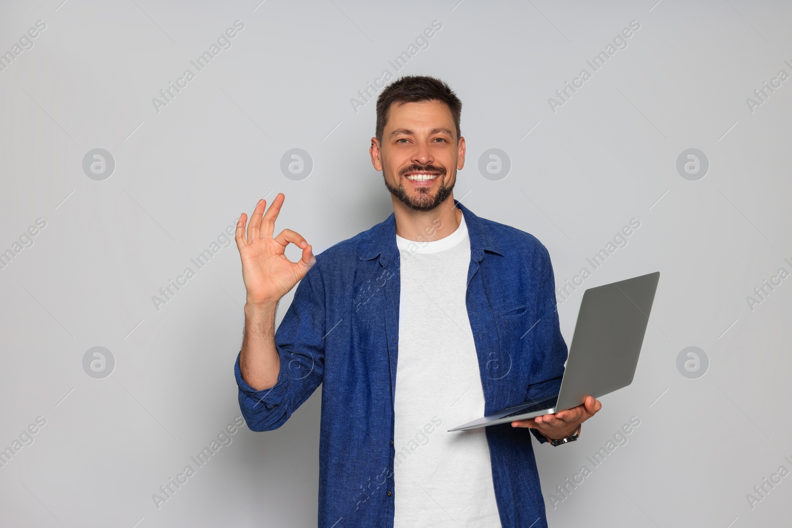 Photo of Smiling man with laptop showing okay gesture on light grey background