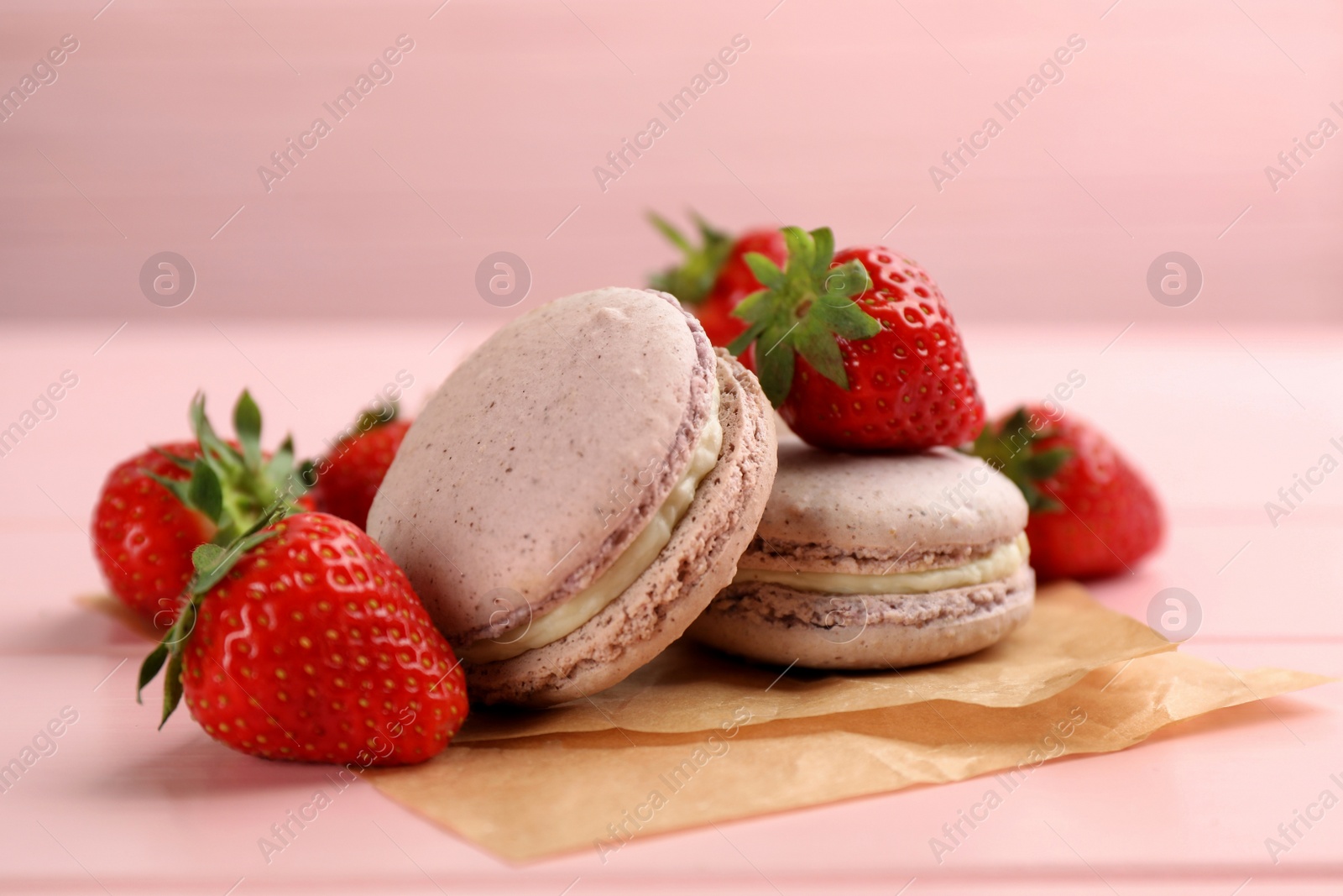 Photo of Delicious macarons and strawberries on pink wooden table, closeup