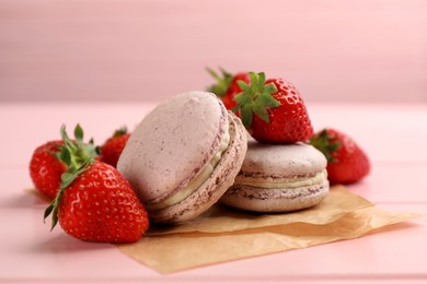 Delicious macarons and strawberries on pink wooden table, closeup