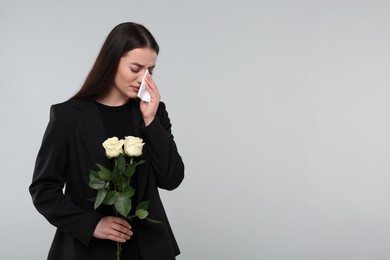 Photo of Sad woman with white rose flowers mourning on light grey background, space for text. Funeral ceremony