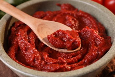 Photo of Bowl of tasty tomato paste with spoon, closeup