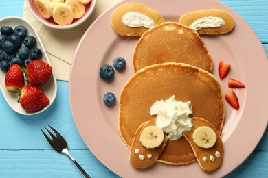 Photo of Creative serving for kids. Plate with cute bunny made of pancakes, berries, cream and banana on light blue wooden table, flat lay