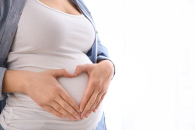 Photo of Young pregnant woman on light background, closeup. Space for text