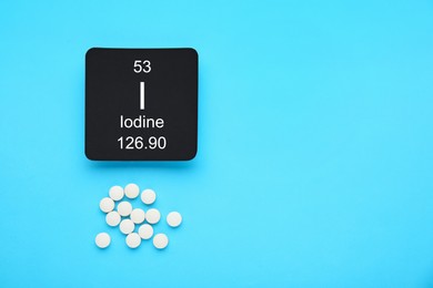 Card with iodine element and pills on light blue background, flat lay. Space for text