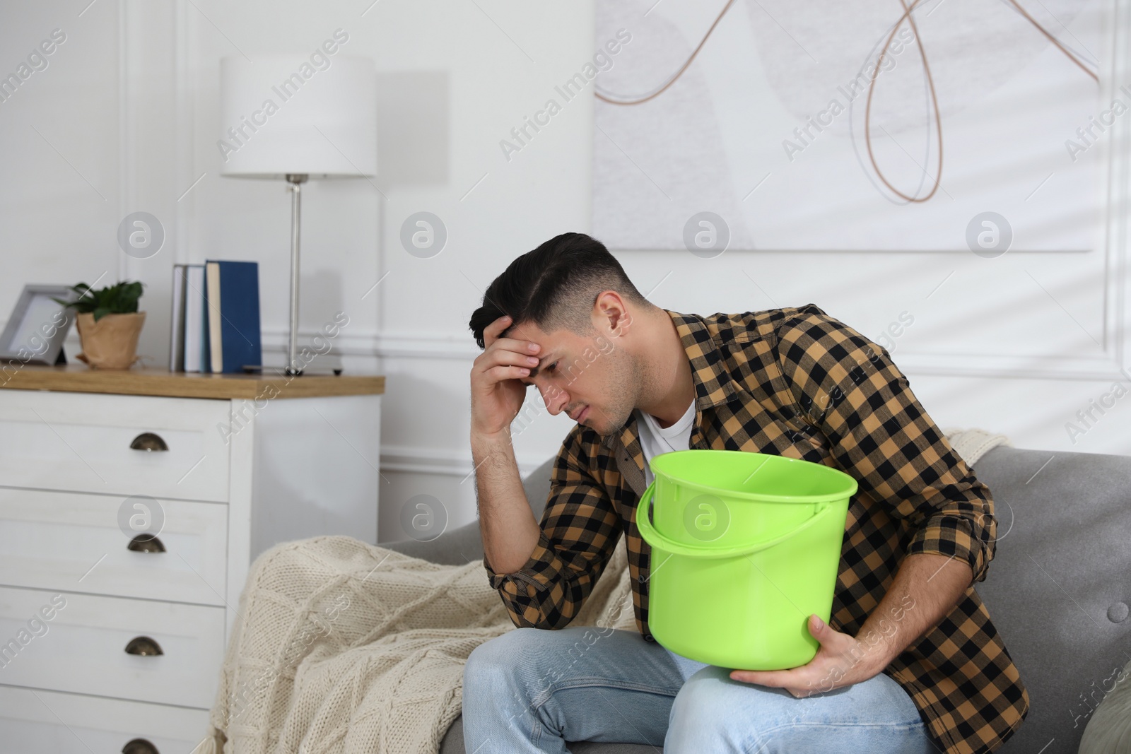 Photo of Emotional man collecting water leaking from ceiling in living room. Damaged roof