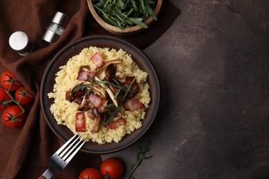 Tasty couscous with mushrooms and bacon in bowl served on brown table, flat lay. Space for text