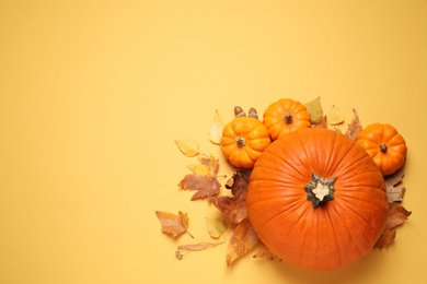 Photo of Flat lay composition with different ripe pumpkins and autumn leaves on yellow background. Space for text