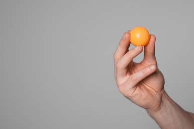 Photo of Man with ping pong ball on light grey background, closeup. Space for text
