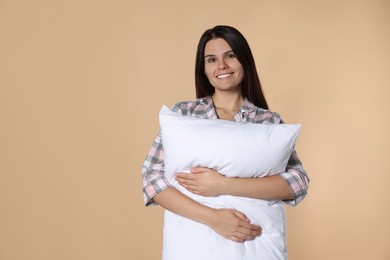 Happy young woman hugging soft pillow on beige background, space for text