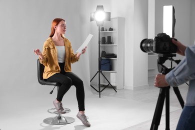 Photo of Casting call. Woman with script performing while camera operator filming her against light grey background in studio