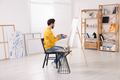 Photo of Man painting in studio. Using easel to hold canvas