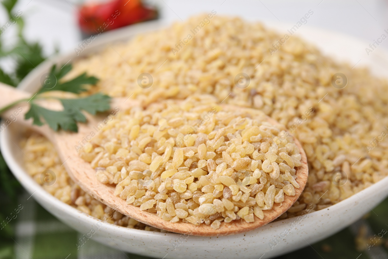 Photo of Bowl and spoon with raw bulgur on table, closeup