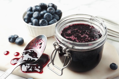 Photo of Jar of blueberry jam and fresh berries on table, closeup