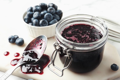 Jar of blueberry jam and fresh berries on table, closeup