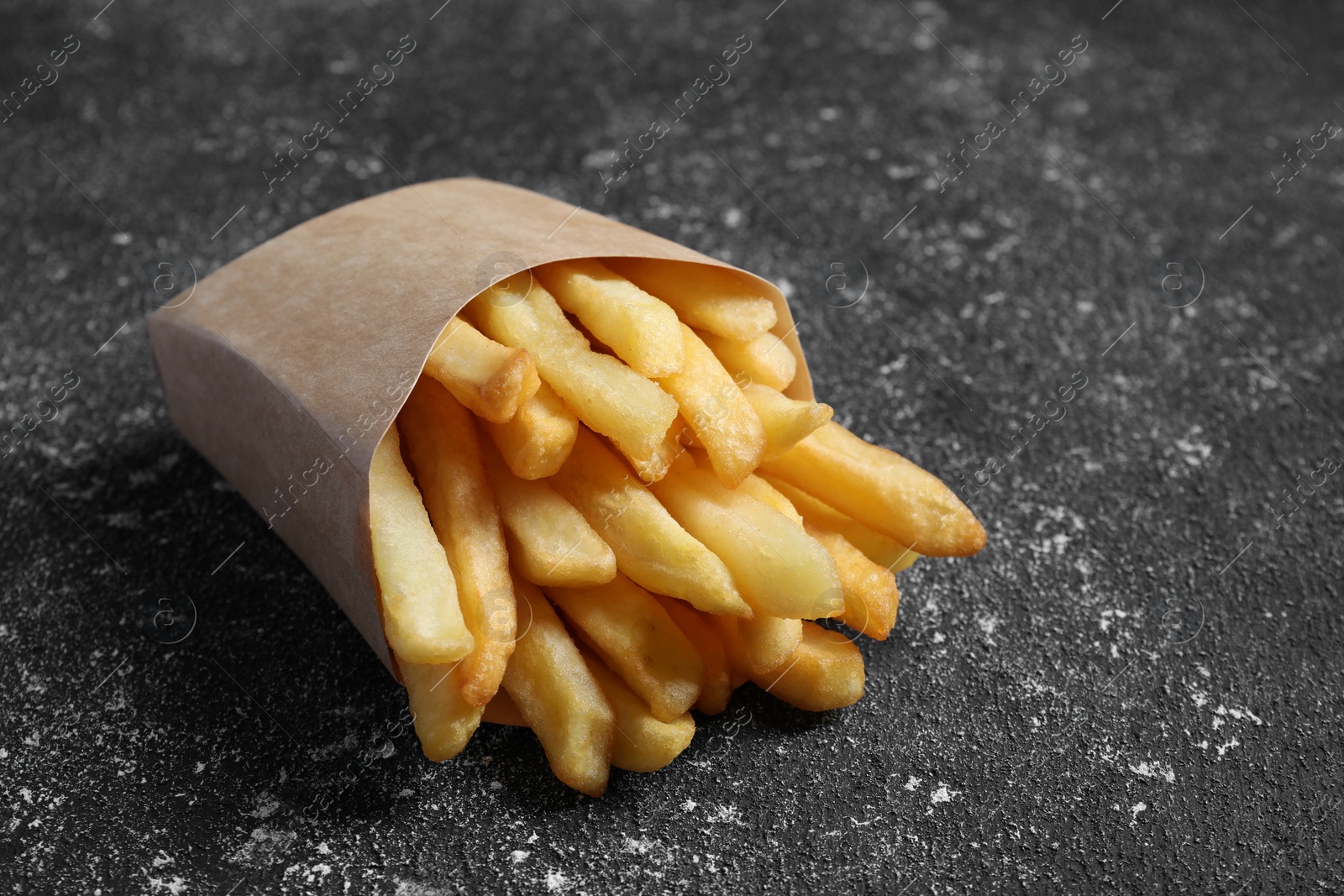 Photo of Delicious french fries in paper box on black textured table, closeup
