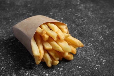 Photo of Delicious french fries in paper box on black textured table, closeup