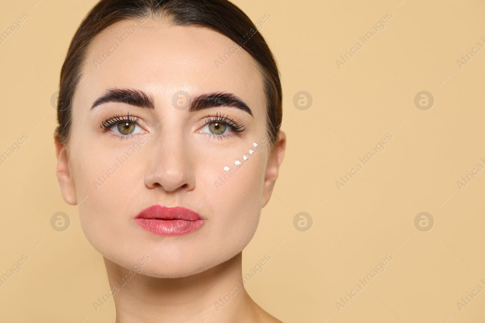 Photo of Woman with cosmetic product around eye on beige background. Space for text