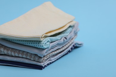 Stack of clean baby clothes on light blue background, closeup. Space for text