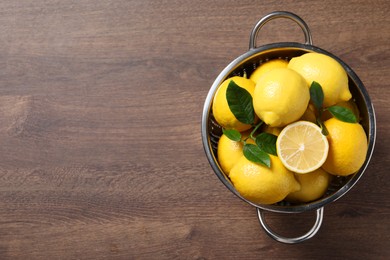 Fresh lemons and green leaves in colander on wooden table, top view. Space for text