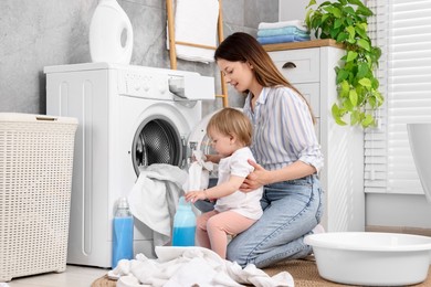 Mother with her daughter washing baby clothes in bathroom