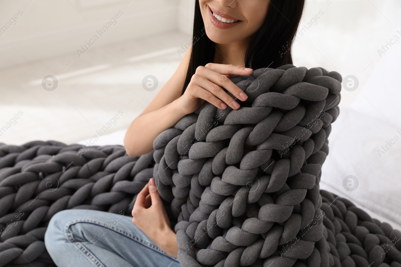 Photo of Woman with chunky knit blanket on bed at home, closeup