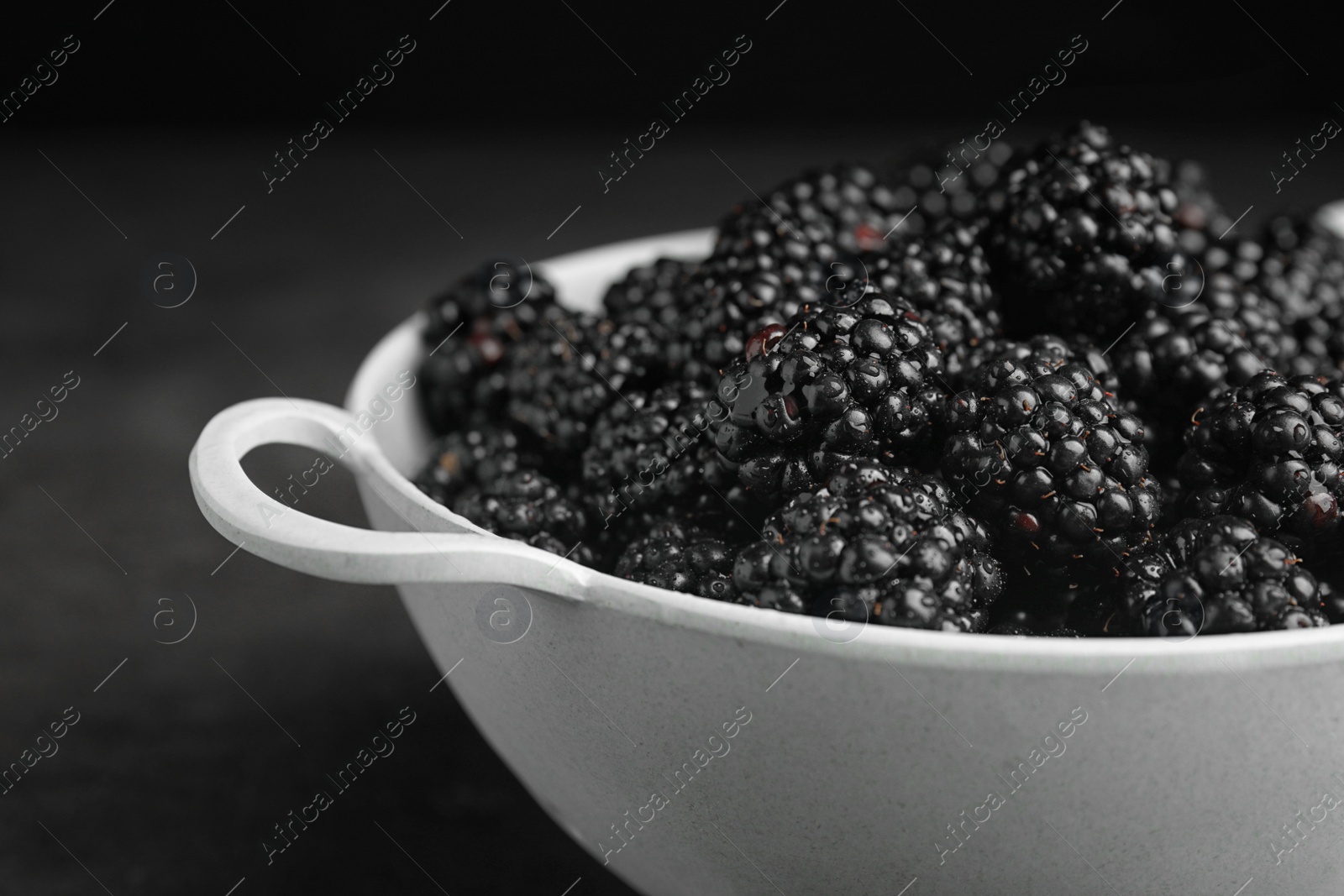 Photo of Colander with tasty ripe blackberries on dark background, closeup