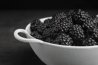 Photo of Colander with tasty ripe blackberries on dark background, closeup