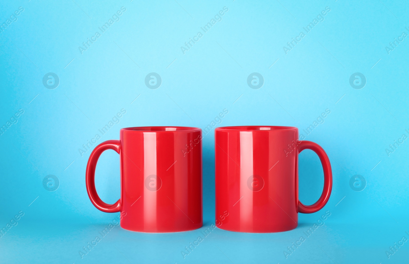 Blank red ceramic mugs on light blue background Photo of Blank red ceramic mugs on light blue background