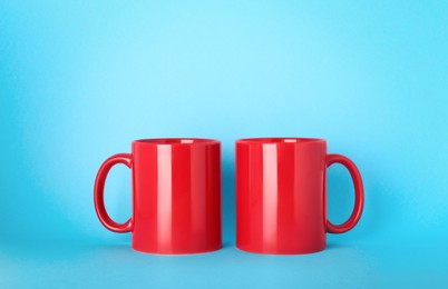 Photo of Blank red ceramic mugs on light blue background