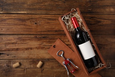 Box with wine bottle, corkscrew and corks on wooden table, flat lay. Space for text