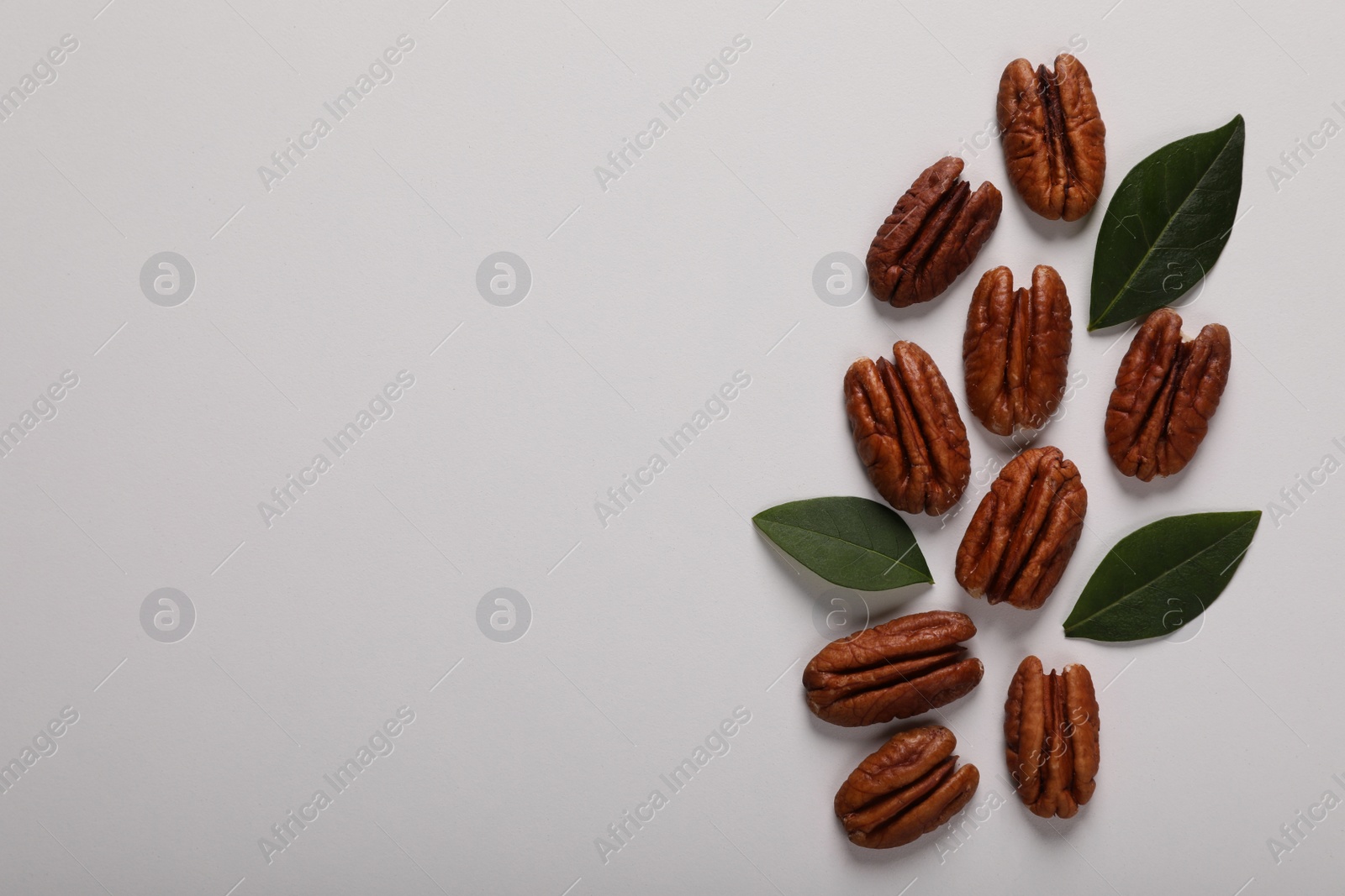 Photo of Delicious pecan nuts and green leaves on white background, flat lay. Space for text