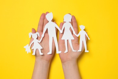 Photo of Woman holding paper family figures on yellow background, top view