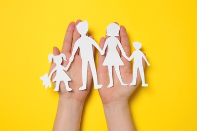 Woman holding paper family figures on yellow background, top view